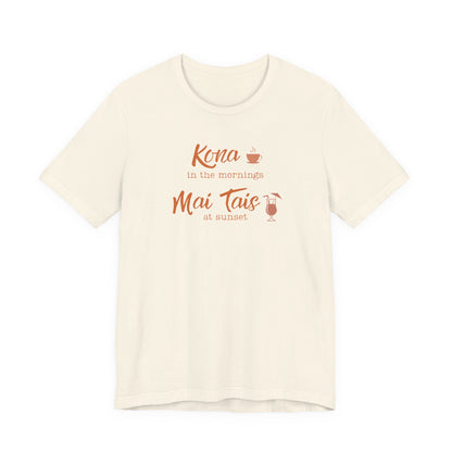An off-white short-sleeve crewneck t-shirt with a coral orange graphic on the chest that reads 'Kona in the mornings Mai Tais at sunset' with small coffee and cocktail illustrations.
