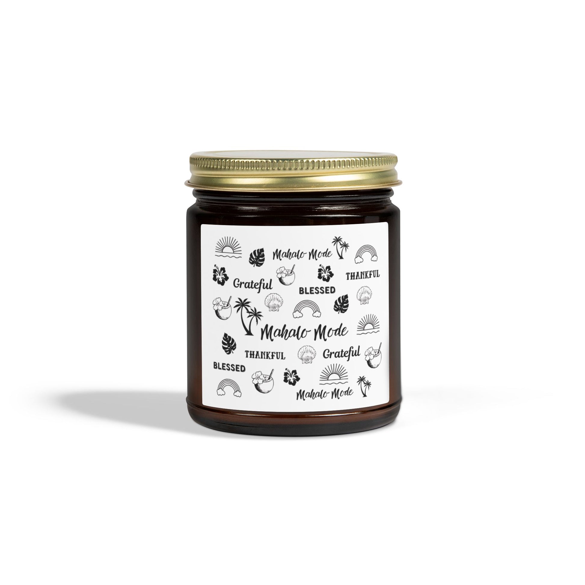 A dark amber glass jar candle with a gold metal screw-on lid and a white paper label featuring black hand-drawn style illustrations and the words 'Mahalo • Mode', 'Grateful', 'BLESSED', and 'THANKFUL'.