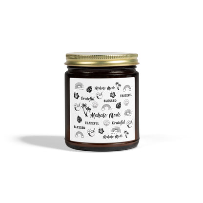 A dark amber glass jar candle with a gold metal screw-on lid and a white paper label featuring black hand-drawn style illustrations and the words 'Mahalo • Mode', 'Grateful', 'BLESSED', and 'THANKFUL'.