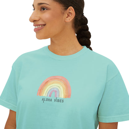 A woman wearing a light aqua blue t-shirt with a pastel rainbow graphic and the text 'ALOHA VIBES' printed on the chest, shown against a plain white background.
