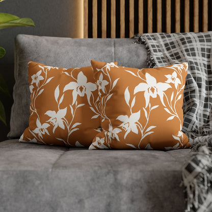 Two square throw pillows with a white orchid vine pattern on a burnt orange background, styled on a gray sofa next to a black and white plaid throw blanket.