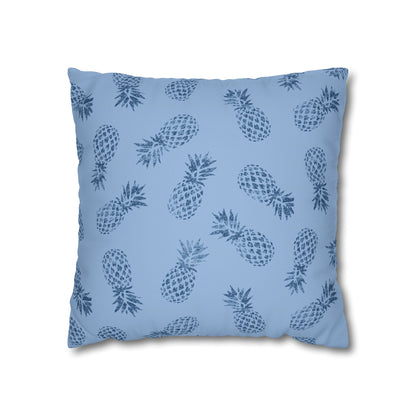 A square throw pillow featuring a repeating dark blue pineapple pattern on a light blue background, shown against a plain white studio backdrop.
