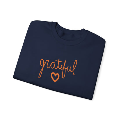 A folded navy crewneck sweatshirt featuring the word 'grateful' in orange cursive script and an orange heart outline on the front, set against a plain white background.