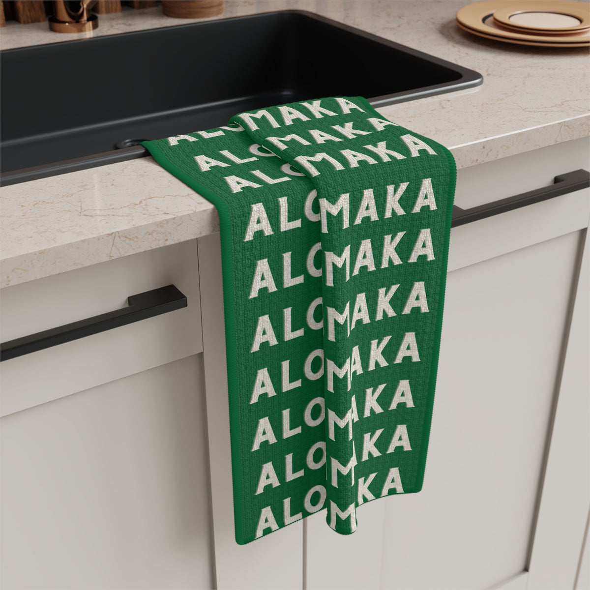 Green Aloha Kalikimaka holiday kitchen towel with repeating cream lettering hanging from a kitchen sink
