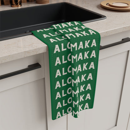 Green Aloha Kalikimaka holiday kitchen towel with repeating cream lettering hanging from a kitchen sink