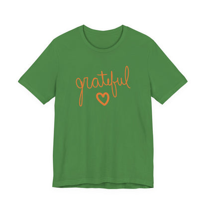 A green short-sleeve crewneck t-shirt featuring the word 'grateful' in orange cursive script and an orange heart outline on the front, displayed against a solid white background.
