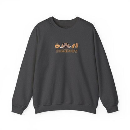 A dark gray crewneck sweatshirt featuring a central graphic of a dog under a blanket, house slippers, coffee cups and the word 'HOMEBODY' printed below it.