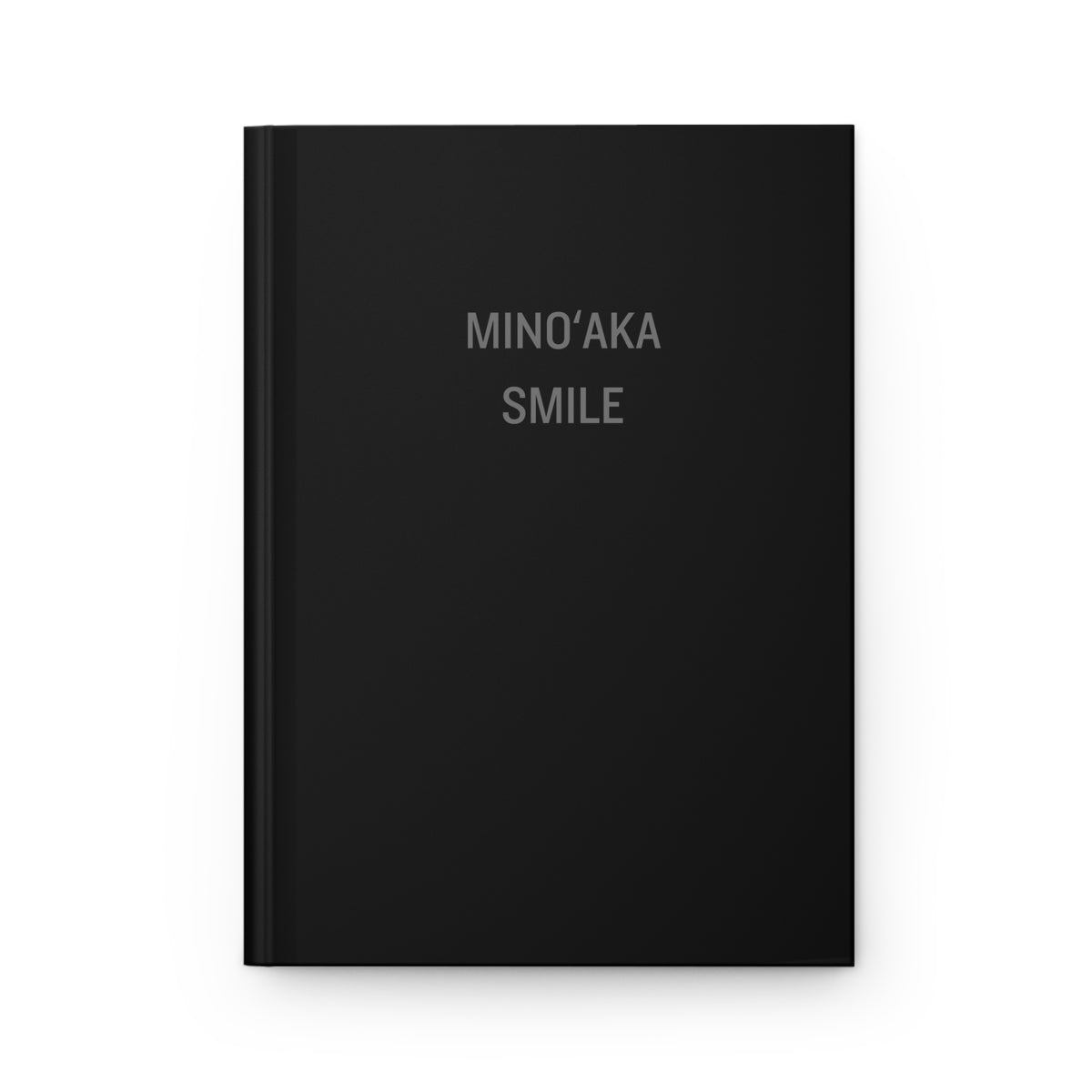 A black hardcover notebook with the words 'MINO'AKA SMILE' printed in a light gray serif font on the front cover, shown against a plain white background.