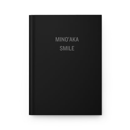 A black hardcover notebook with the words 'MINO'AKA SMILE' printed in a light gray serif font on the front cover, shown against a plain white background.