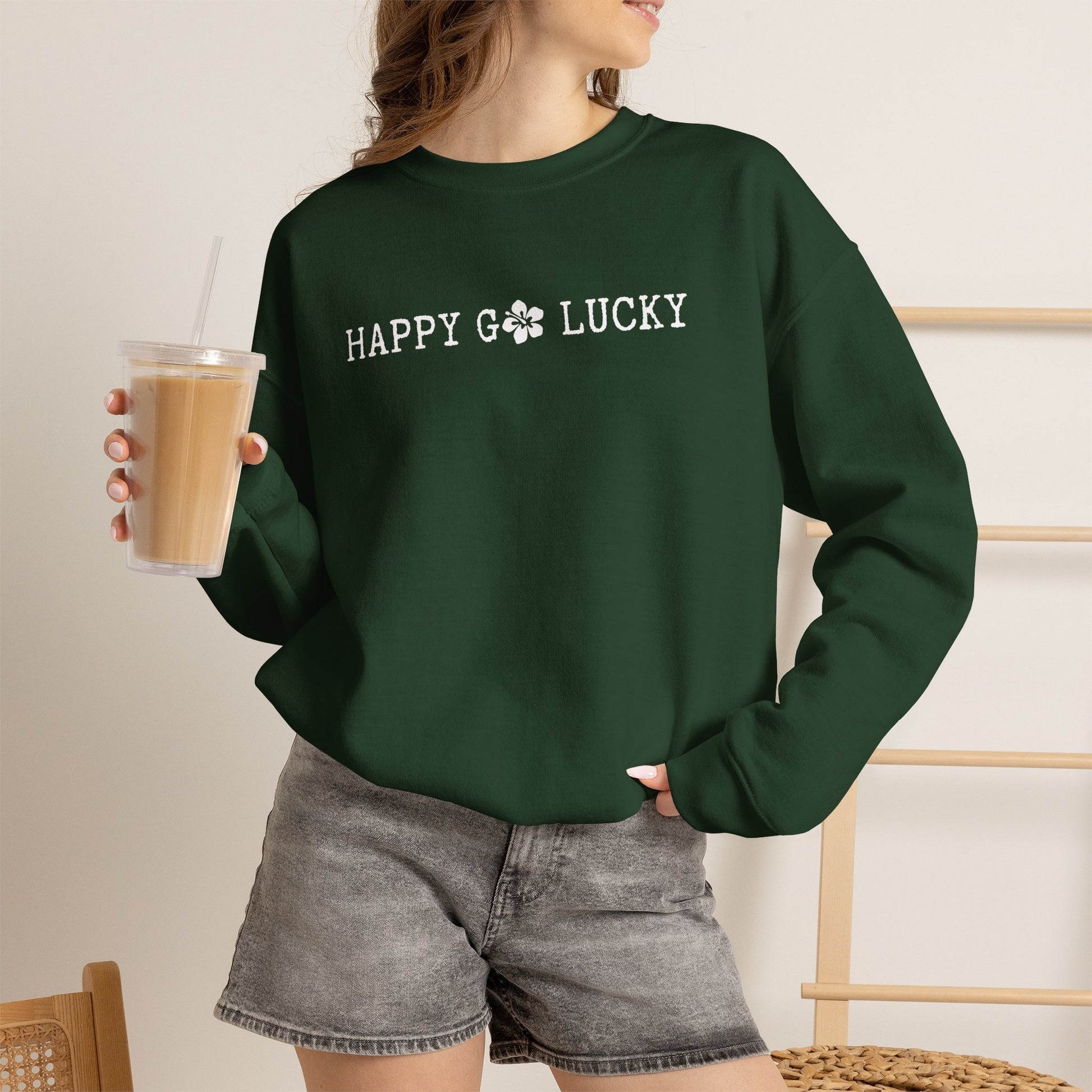 Person wearing a GREEN sweatshirt with text ʻHAPPY GO LUCKYʻ, holding a drink.