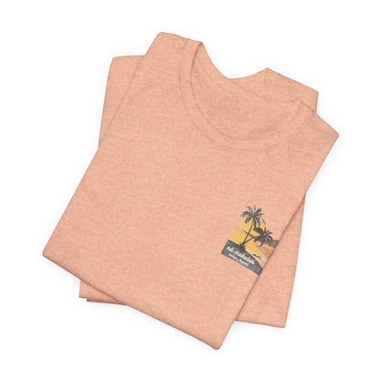 A heather peach short-sleeve t-shirt with a vintage-style graphic on the front left chest depicting two palm trees against a yellow and orange sunset, with the text 'ná makulua' and 'Kailua, Hawaii!' printed below.