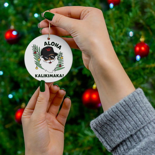 White ceramic ornament featuring Santa in sunglasses and black shaka hat with tropical greenery and Aloha Kalikimaka lettering.