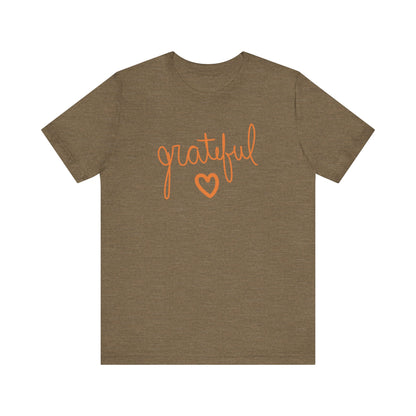 A heather olive short-sleeve t-shirt with the word 'grateful' written in orange cursive script and a matching orange heart outline on the chest, displayed against a solid white background.