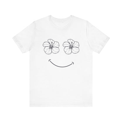 A white short-sleeve crewneck t-shirt featuring a minimalist graphic of two black-outlined hibiscus flowers for eyes and a simple black smile on the front.