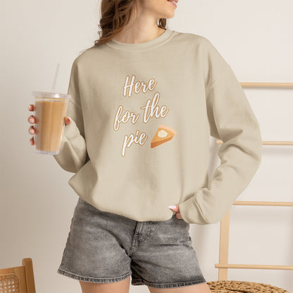 A woman wearing a sand crewneck sweatshirt with a graphic that reads 'Here for the pie' in brown script next to a slice of pie, paired with gray denim shorts and holding an iced coffee.