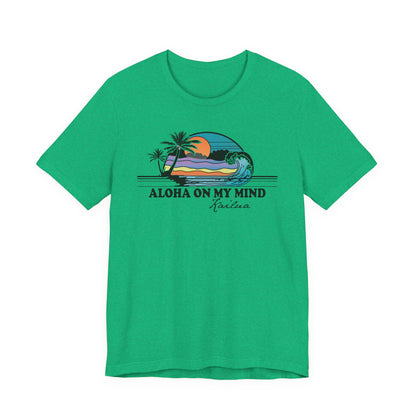A green short-sleeve crewneck t-shirt featuring a retro graphic of a beach sunset with palm trees and the text 'ALOHA ON MY MIND' and 'Kailua' printed on the chest.