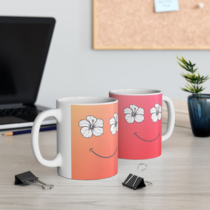 Two ceramic mugs with white handles and bases, decorated with a white hibiscus flower and smiley face design over a peach-to-pink gradient, displayed on a light wood desk with office props in the background.