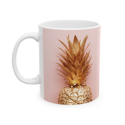 A white ceramic mug featuring a printed design of a pineapple with a metallic gold finish on its body and a light pink background, shown on a solid white background.
