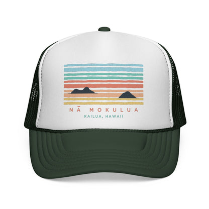A white and dark green trucker hat with a colorful sunset graphic on the front panel that reads 'NÁ MOKULUA KAILUA, HAWAII'.