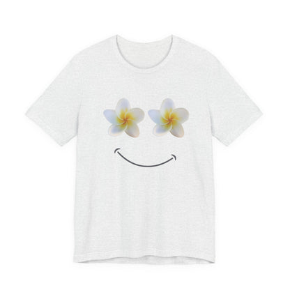 An ash white short-sleeve crewneck t-shirt featuring a graphic of two plumeria flowers acting as eyes and a simple black smiley face below, displayed on a clean white background.