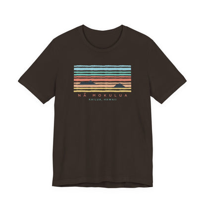 A dark brown short-sleeve t-shirt with a retro sunset graphic on the chest featuring horizontal stripes in light blue, teal, orange, and red, with the text 'NA MOKULUA KAILUA, HAWAII' printed below.