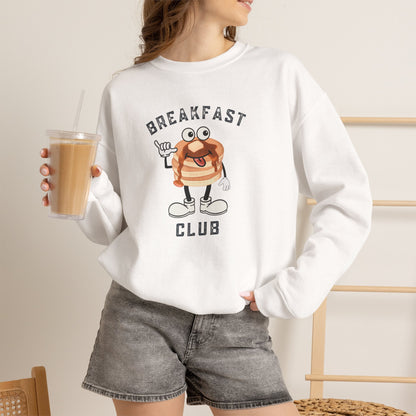 A woman wearing a white crewneck sweatshirt with a cartoon pancake graphic and the text 'BREAKFAST CLUB', paired with gray denim shorts and holding an iced coffee.