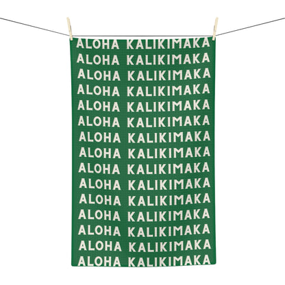 Green Aloha Kalikimaka holiday kitchen towel with repeating cream lettering
