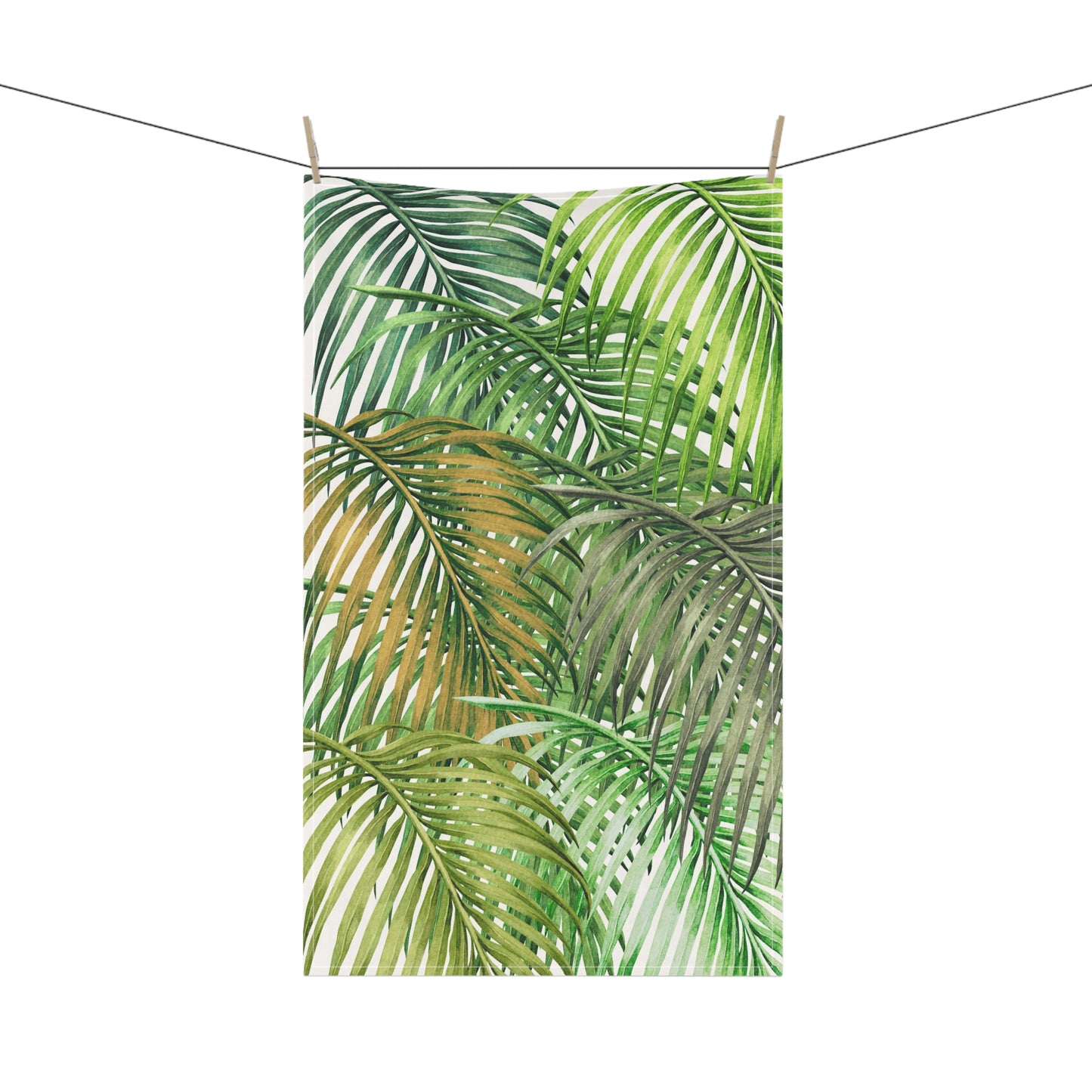 A rectangular tea towel featuring a watercolor tropical palm leaf pattern in shades of green and yellow, hanging from a string with two wooden clothespins against a plain white background.