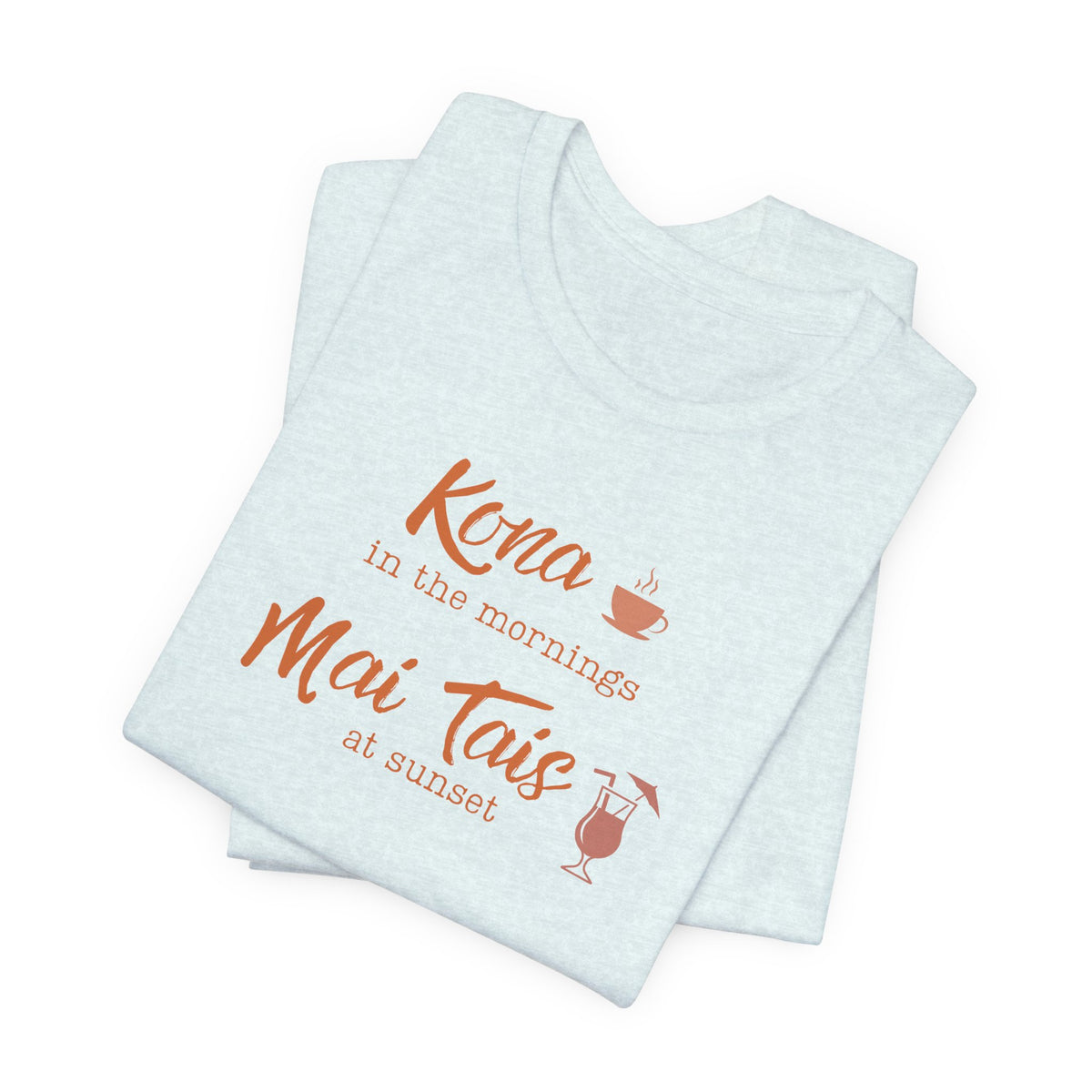 A folded light heather blue t-shirt with a coral orange graphic print that reads 'Kona in the mornings Mai Tais at sunset' with a coffee cup and cocktail glass illustration, set against a plain white background.