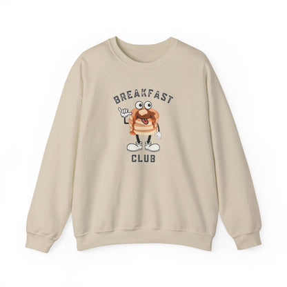 A sand crewneck sweatshirt featuring a cartoon graphic of a breakfast stack of pancakes character with the text 'BREAKFAST CLUB' printed on the front, displayed against a clean white background.