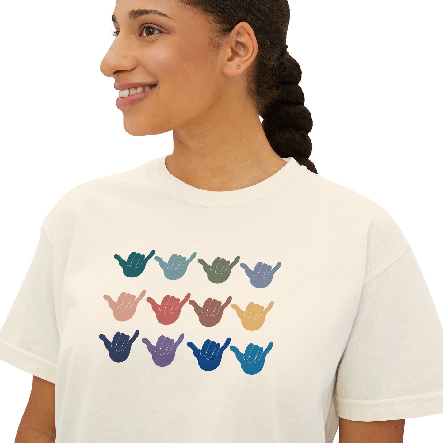 A woman wearing a white crewneck t-shirt with a graphic of twelve shaka signs in various colors arranged in a grid.