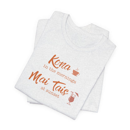 A folded light heather gray t-shirt with orange text reading 'Kona in the mornings Mai Tais at sunset' and small orange coffee and cocktail graphics, shown on a white background.