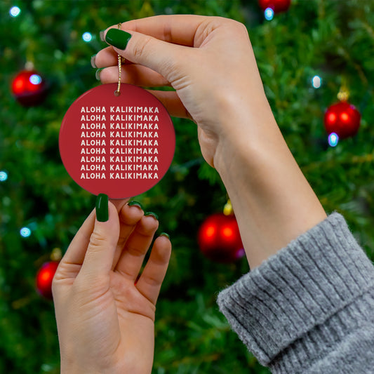 Red ceramic Christmas ornament featuring repeating cream Aloha Kalikimaka lettering on both sides.