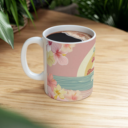A white ceramic coffee mug with a retro Hawaiian-themed print, filled with coffee and resting on a light wooden table with green plants in the background.