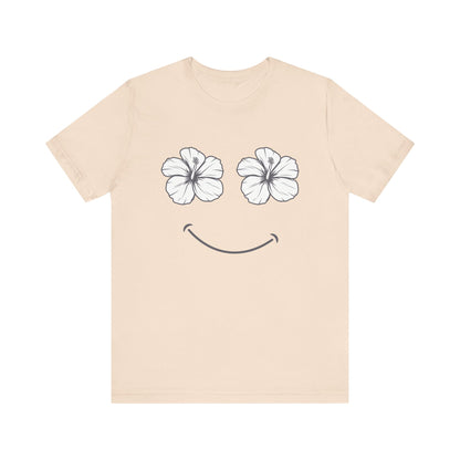 A light beige crewneck t-shirt featuring a graphic of two white hibiscus flowers forming eyes and a simple smile on the front, displayed against a solid white background.
