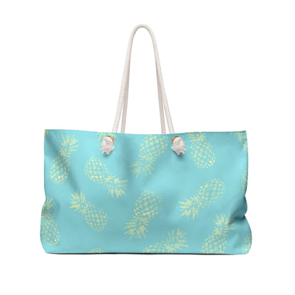A light blue tote bag with a repeating yellow pineapple print and white rope handles, shown against a plain white background.