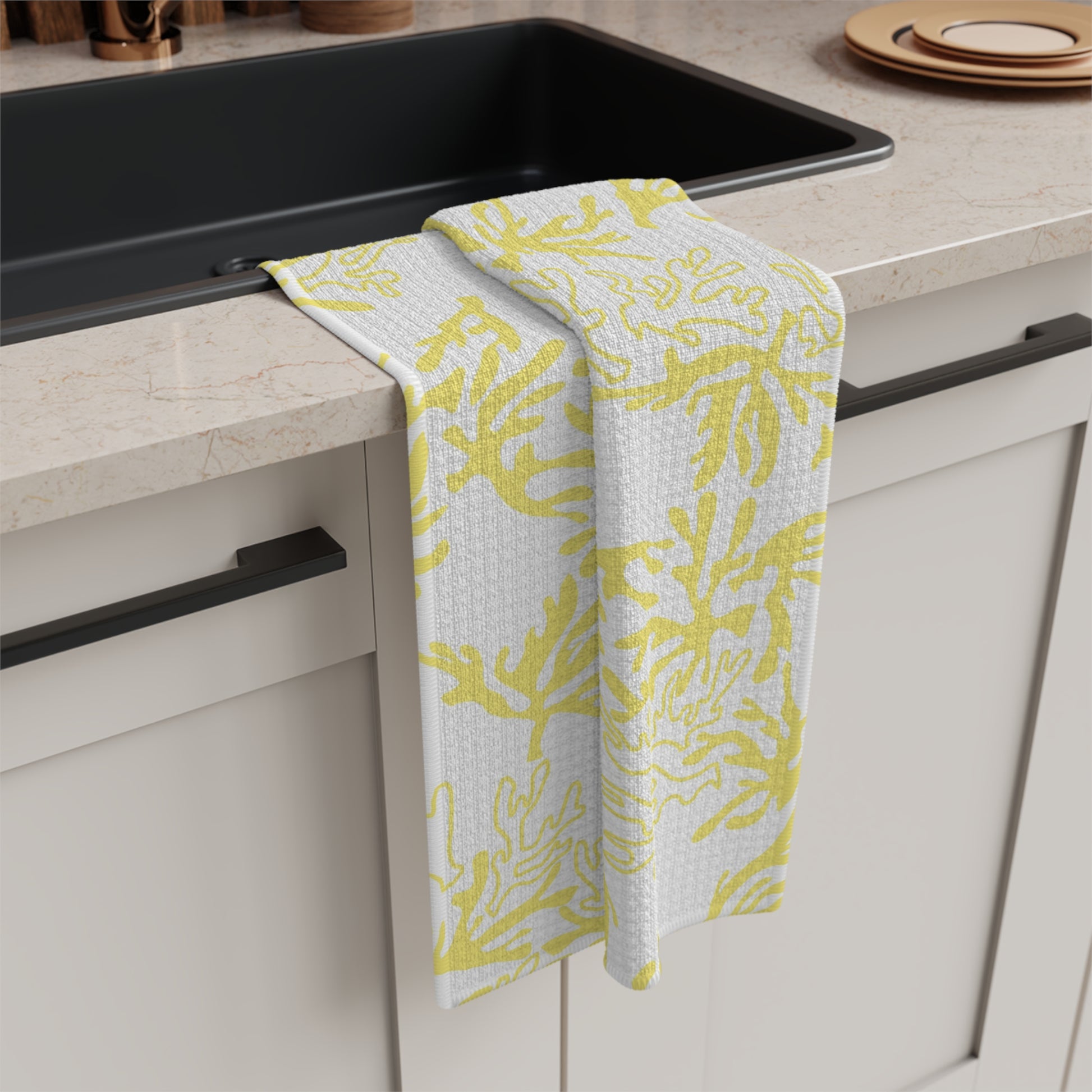 A kitchen towel with a yellow and white coral pattern draped over the edge of a black sink in a modern kitchen setting.
