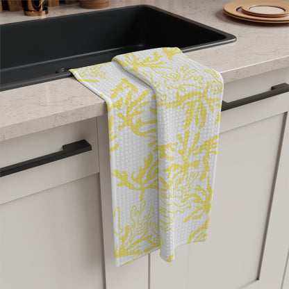 A kitchen towel with a yellow and white coral pattern draped over the edge of a black sink in a modern kitchen setting.