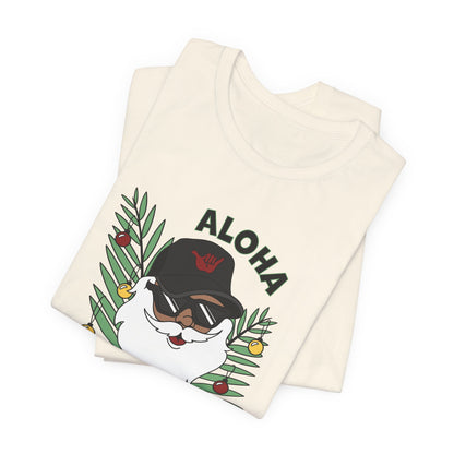 Folded Natural Santa Kalikimaka unisex T-shirt with hand-drawn Santa wearing sunglasses and throwing a shaka surrounded by tropical palm leaves.