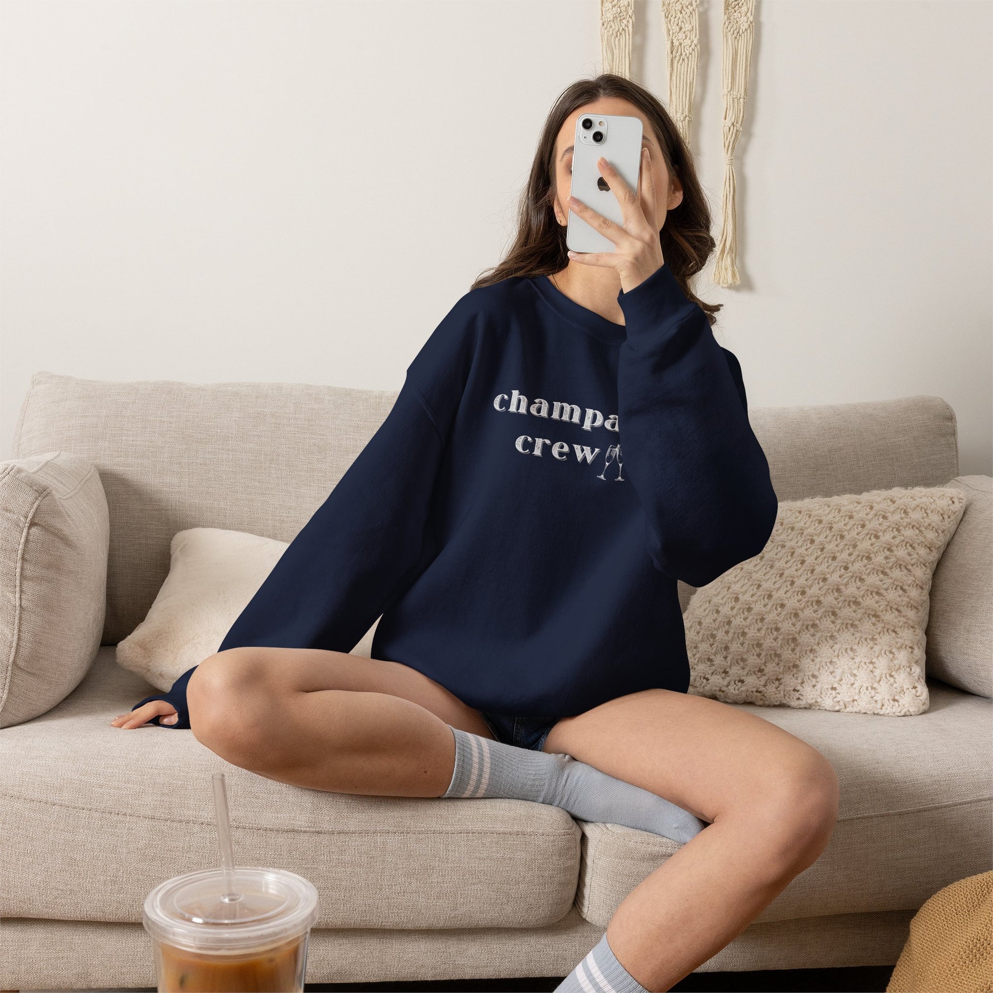 Person wearing a navy sweatshirt with a graphic print 'champagne crew', sitting on a couch in a living room.