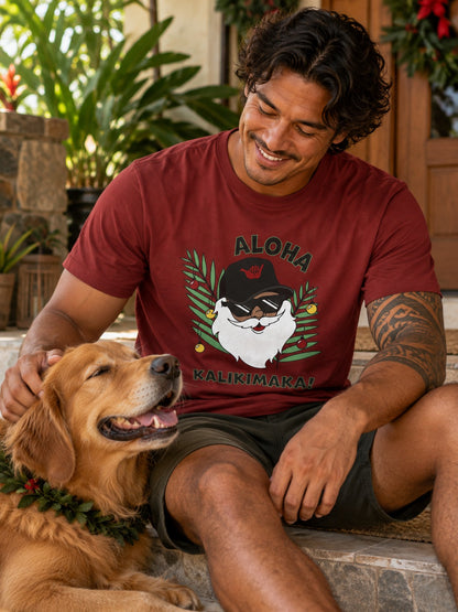 Man wearing red Aloha Kalikimaka Santa graphic tee sitting with a golden retriever on a tropical holiday porch.