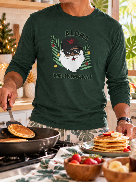 Man wearing a forest green Aloha Kalikimaka long sleeve Christmas tee while making pancakes in a bright tropical kitchen.