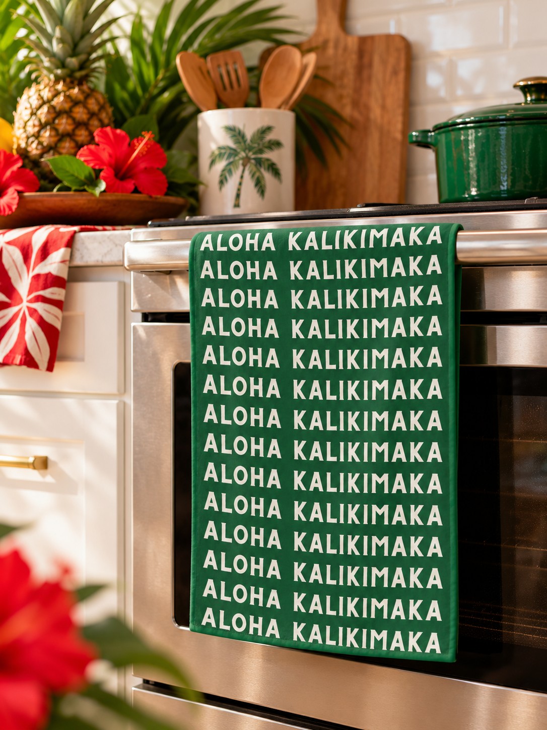 Aloha Kalikimaka Tropical Kitchen — Green Aloha Kalikimaka kitchen towel hanging from an oven in a bright tropical holiday kitchen.