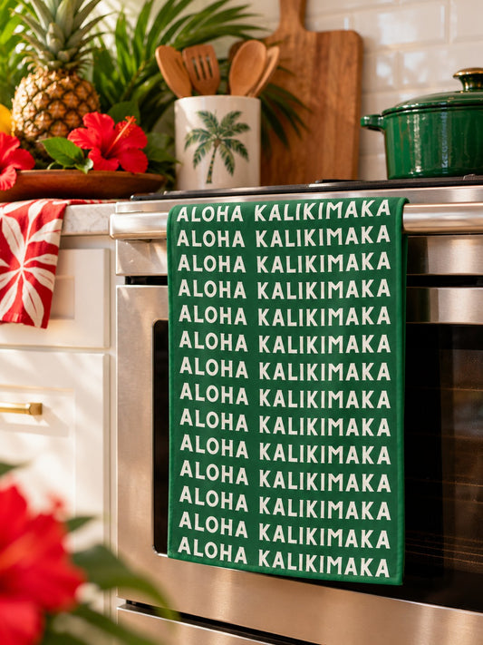 Aloha Kalikimaka Tropical Kitchen — Green Aloha Kalikimaka kitchen towel hanging from an oven in a bright tropical holiday kitchen.