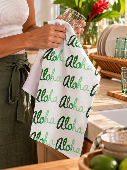 Green Aloha Kitchen Towel — Woman drying a glass with a green Aloha print kitchen towel in a bright island-inspired kitchen.