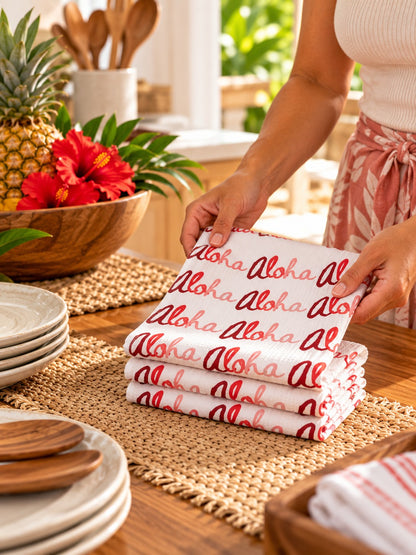 Red Aloha Kitchen Towels — Woman folding red Aloha print kitchen towels on a woven mat in a warm tropical kitchen.