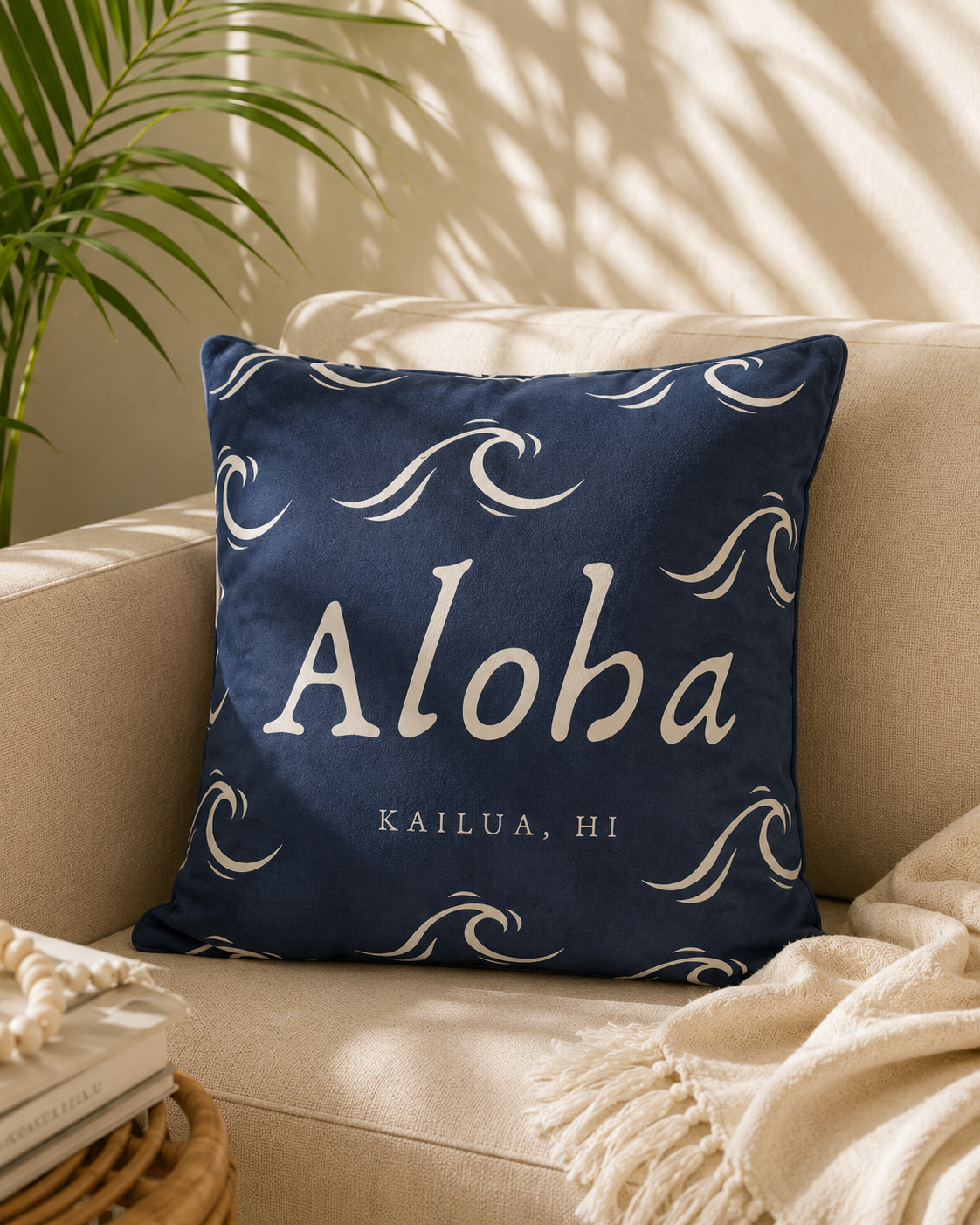 Navy blue pillow with 'Aloha Kailua, HI' text and wave graphic design on a beige couch.