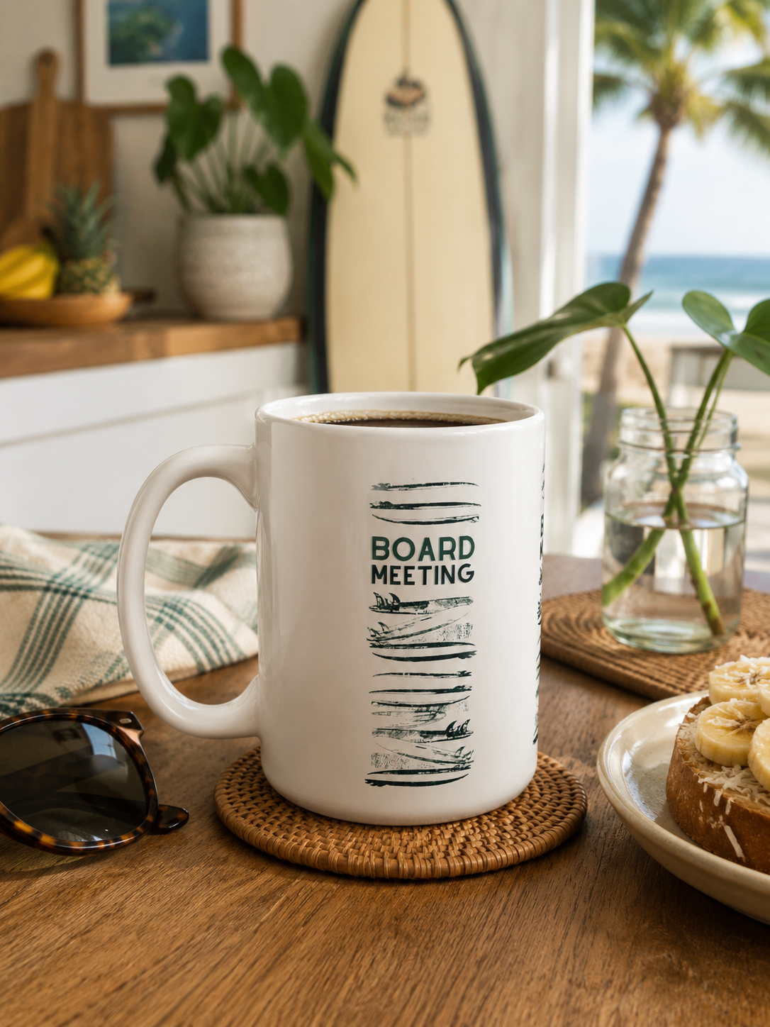 A white ceramic coffee mug with 'BOARD MEETING' printed in dark green on the side, sitting on a woven coaster on a wooden table in a bright, tropical-themed room.