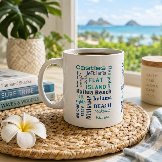 A white ceramic mug printed with various beach and island names in blue and teal text, styled on a woven placemat with a white flower, books, and a jar in a beach-view setting.