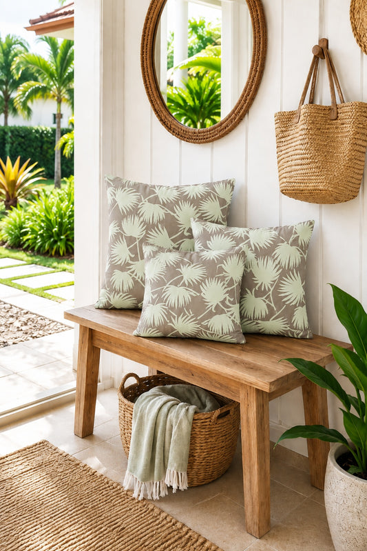 3 square throw pillows featuring an all-over palm frond pattern in sage green on a warm taupe-brown background, shown on a bench at the entryway to a tropical house
